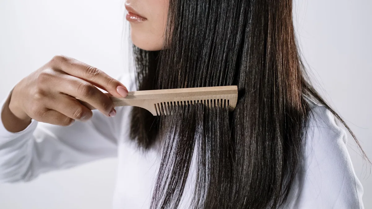 Woman combing her hair gently with a wooden comb