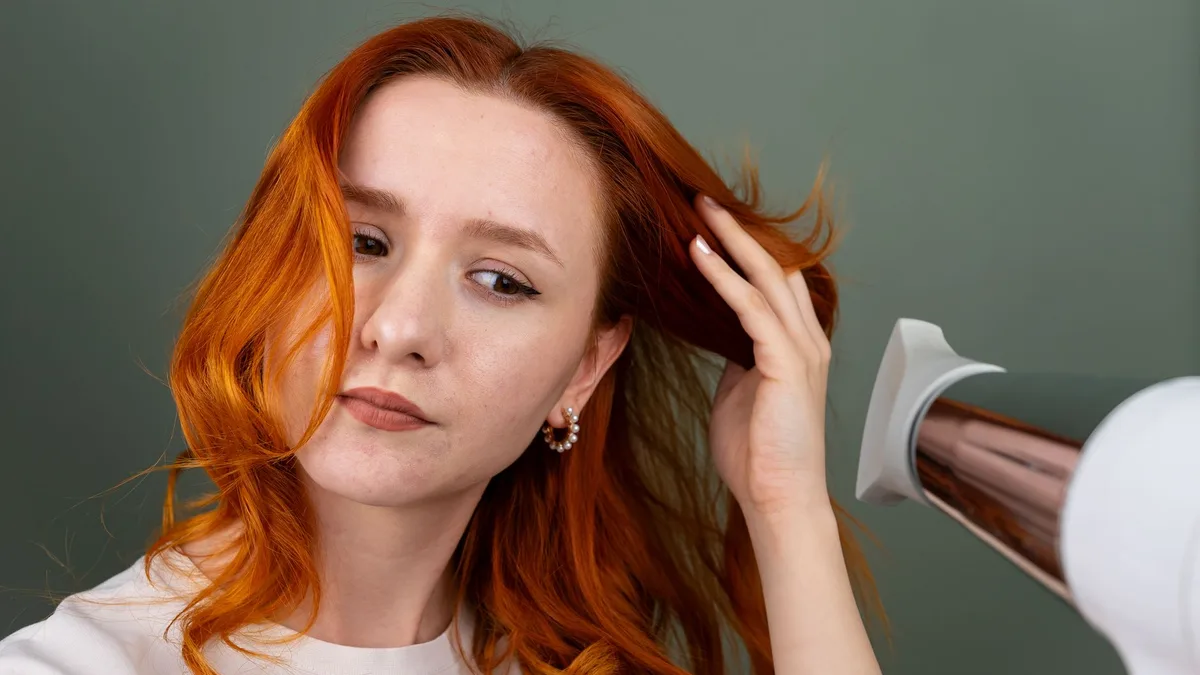 Woman drying her long hair with a hairdryer at home