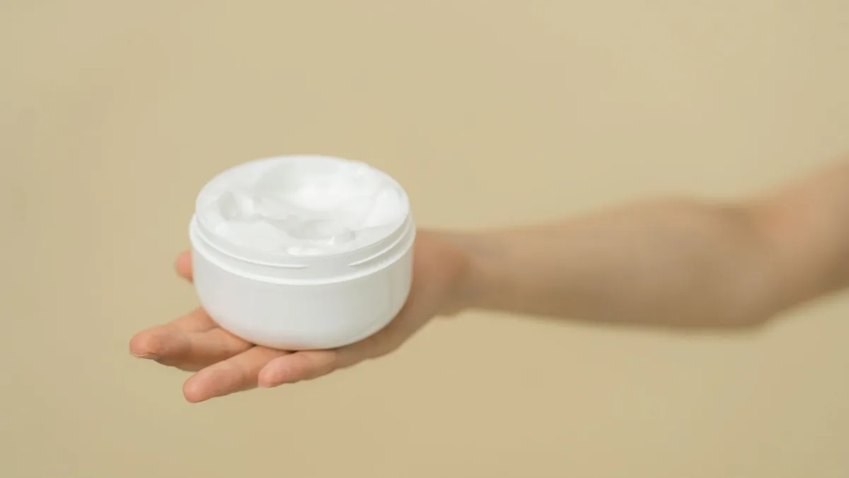 Hand holding an open white jar of curl defining cream