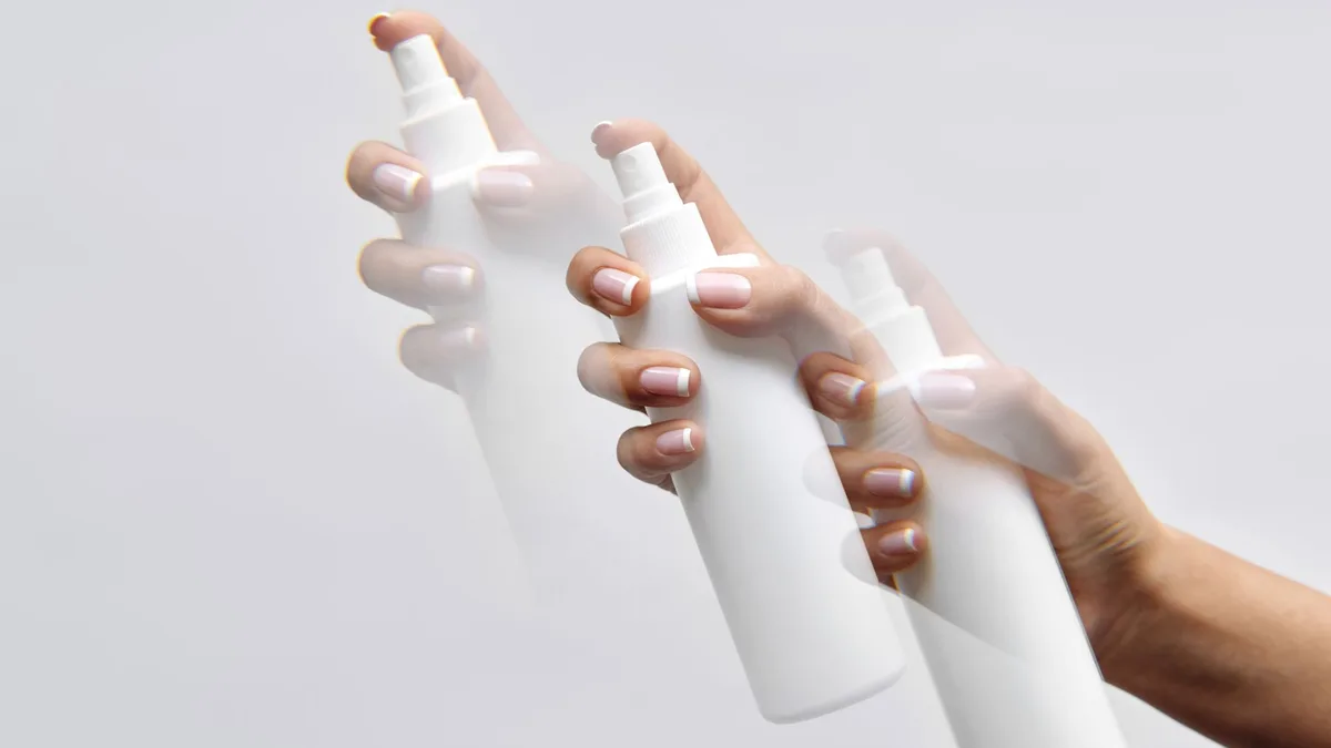 Hand holding a white spray bottle against a plain background