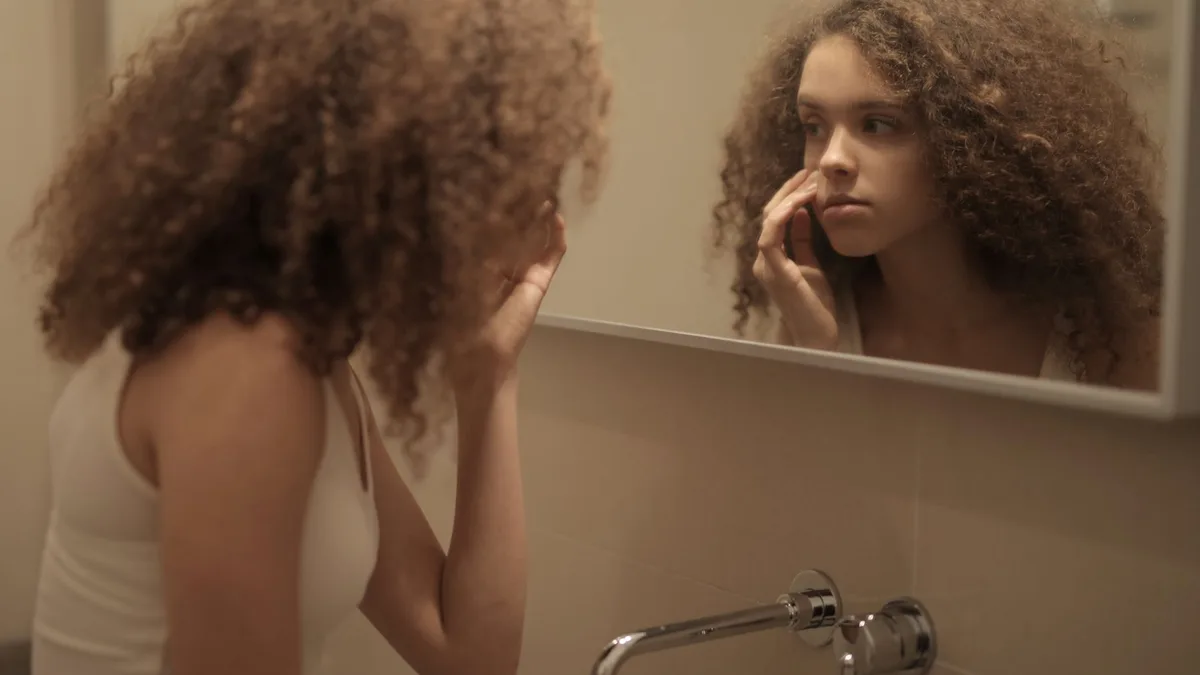 Young woman with curly hair checking her hair in the bathroom mirror