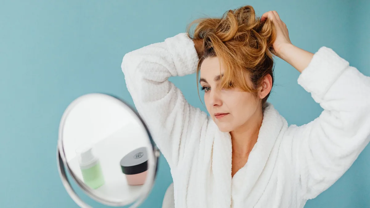 Woman in a bathrobe styling her hair in front of a mirror