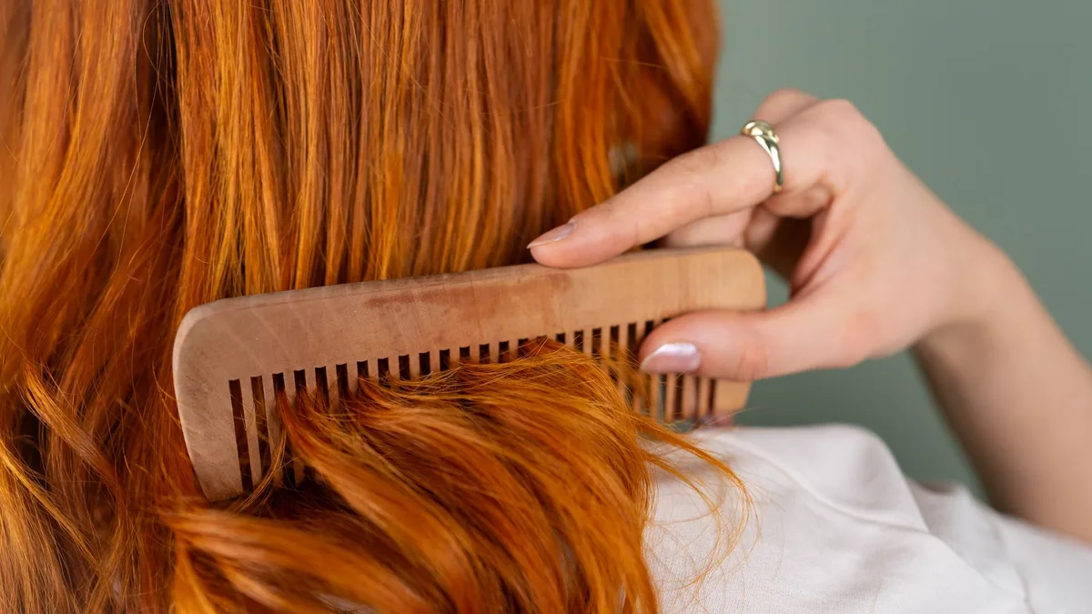 Woman combing her long hair gently with a wide-tooth wooden comb