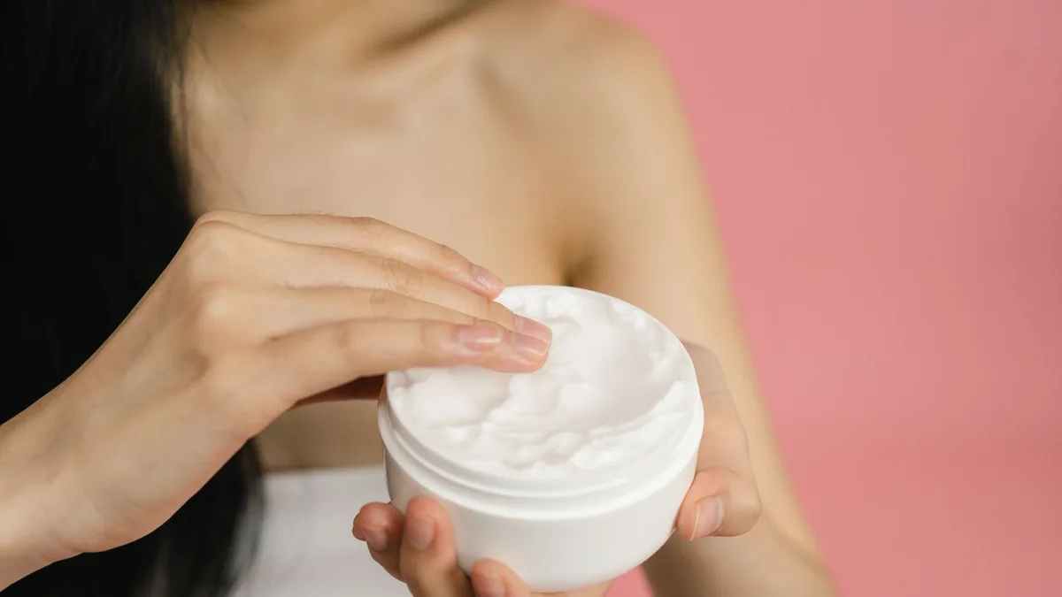 Close-up of hands scooping curl cream from a white jar