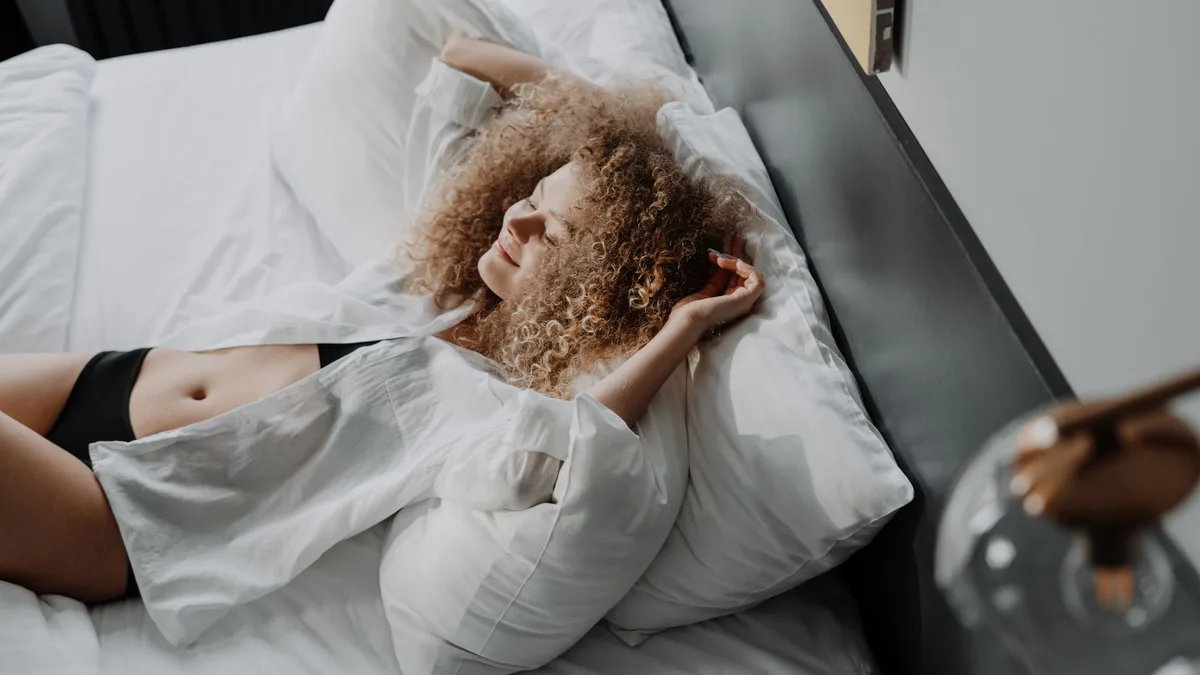 Woman with curly hair resting on a bed in a sunlit bedroom