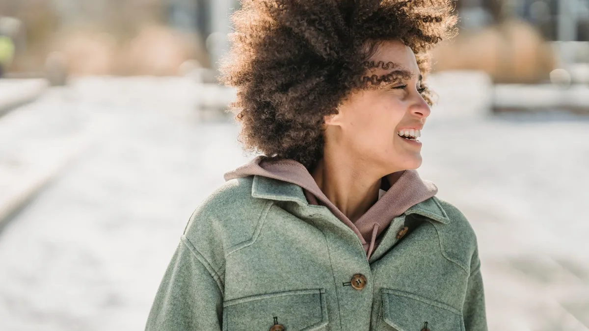Woman with curly hair laughing outdoors in a coat
