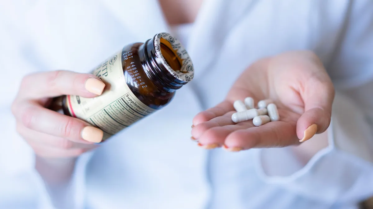Hands holding a supplement bottle and capsules