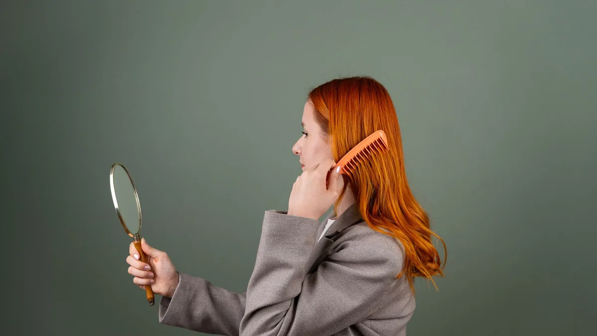 Side profile of a woman checking her hair in a handheld mirror