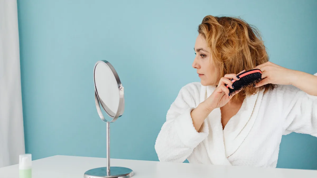 Woman combing her hair in front of a mirror
