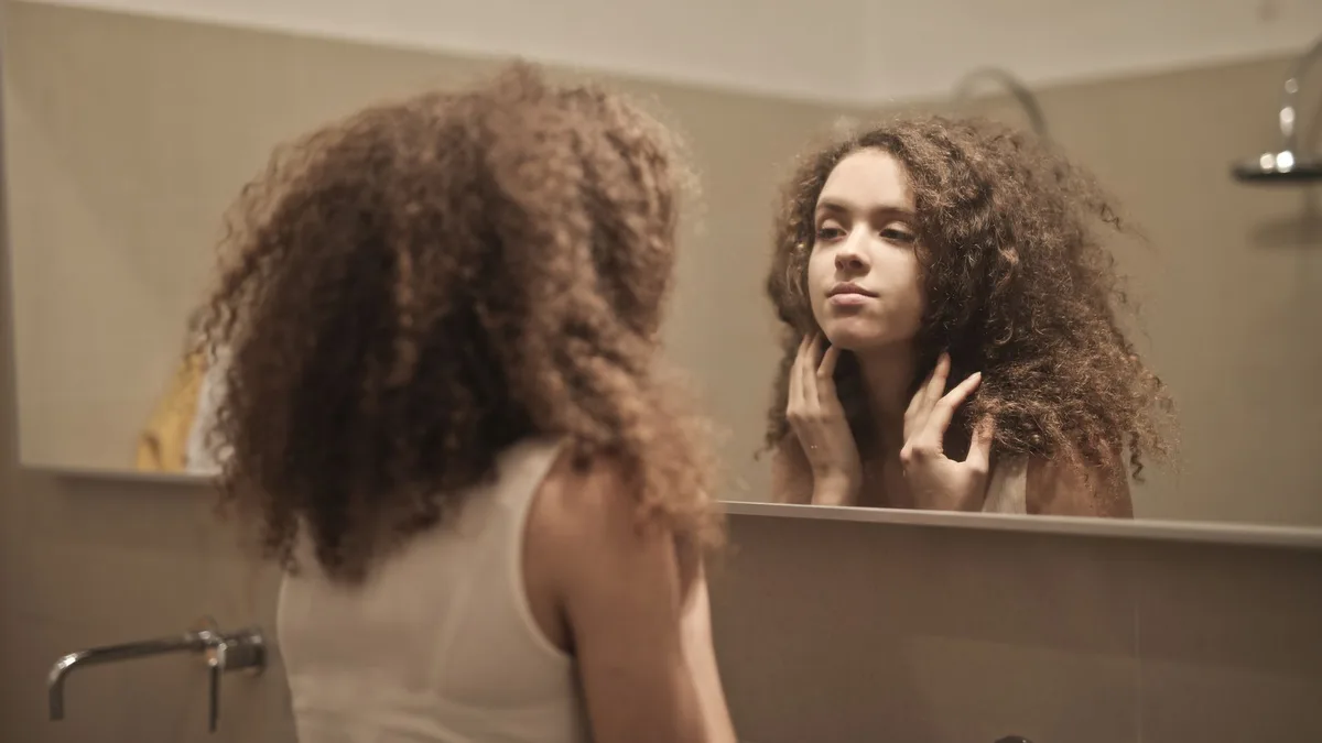 Woman looking thoughtfully into a bathroom mirror