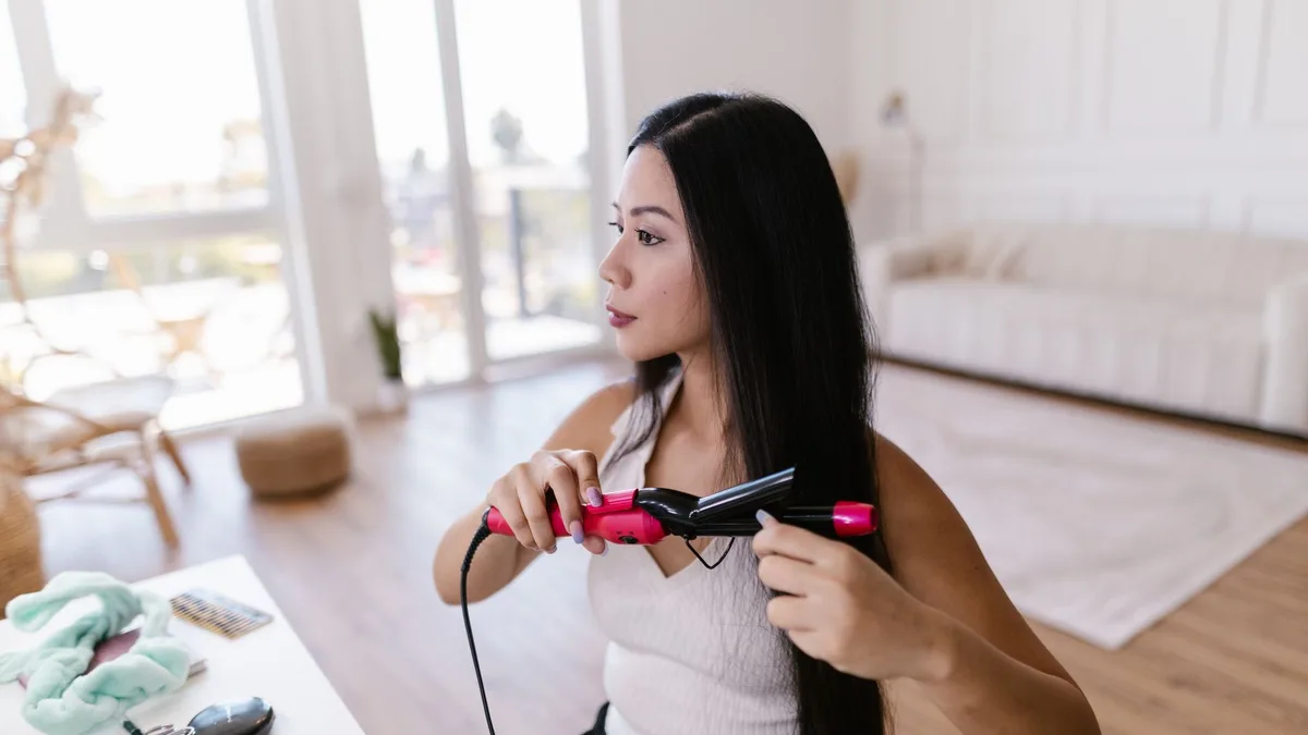 Woman straightening her hair at home with a flat iron