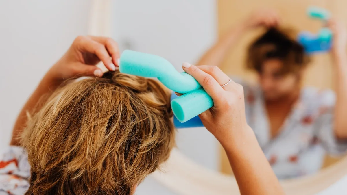 Woman using a curling tool on her hair in front of a mirror