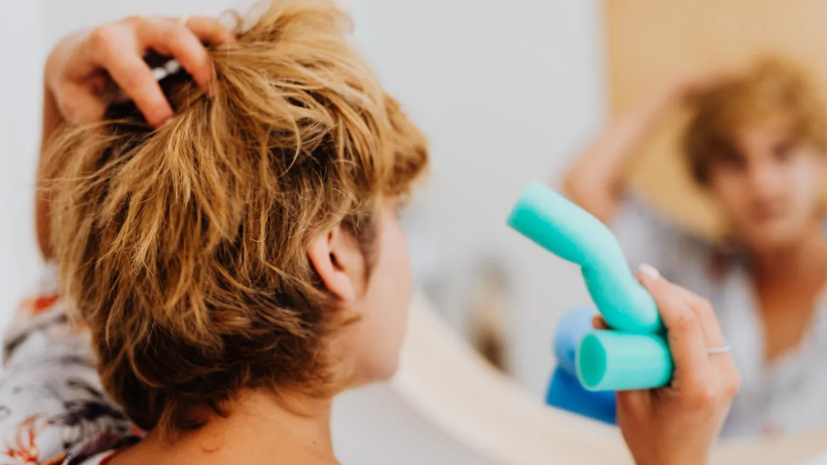Woman putting curlers in her hair in front of a mirror