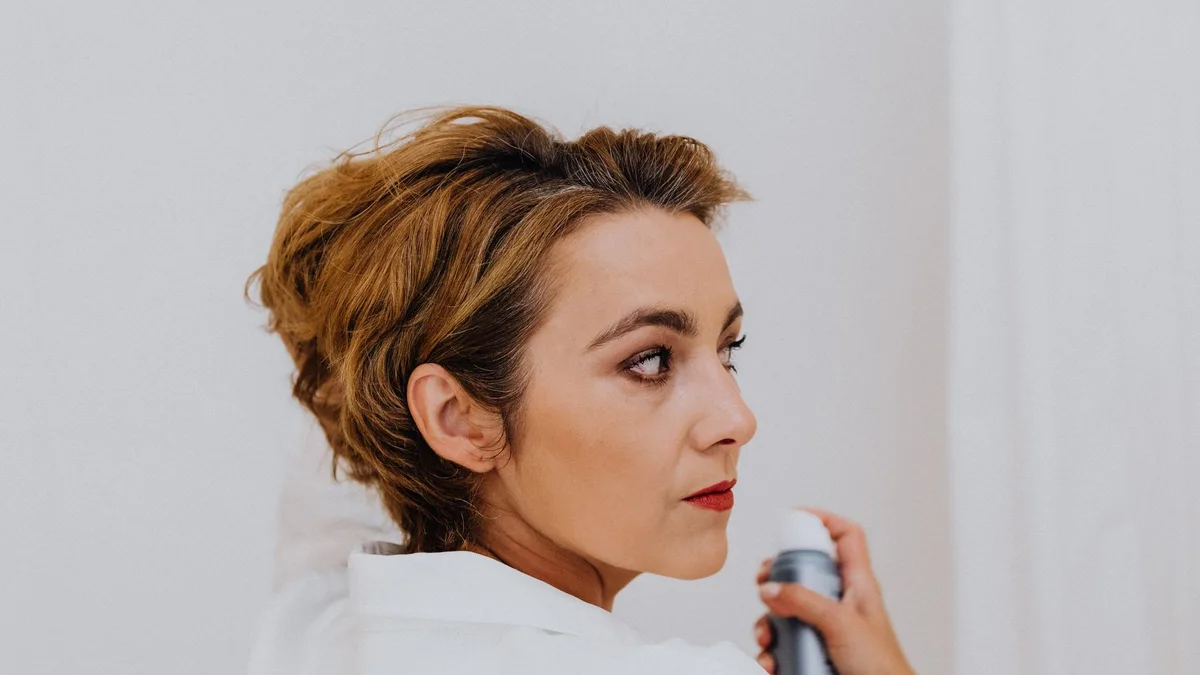 Woman applying hairspray to her short styled hair