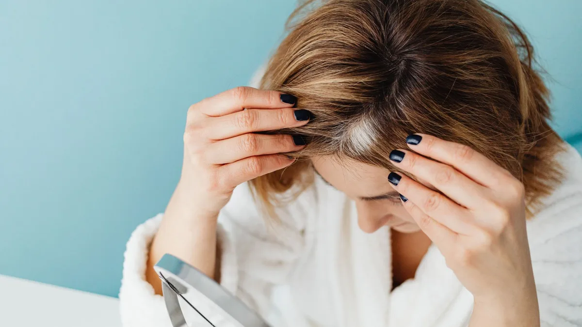 Woman checking her scalp and hair parting in a mirror