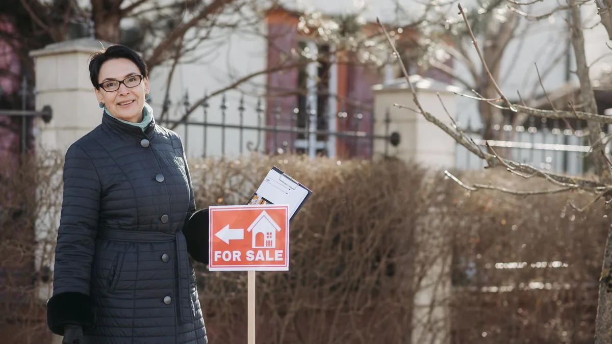 Smiling estate agent beside a for sale sign