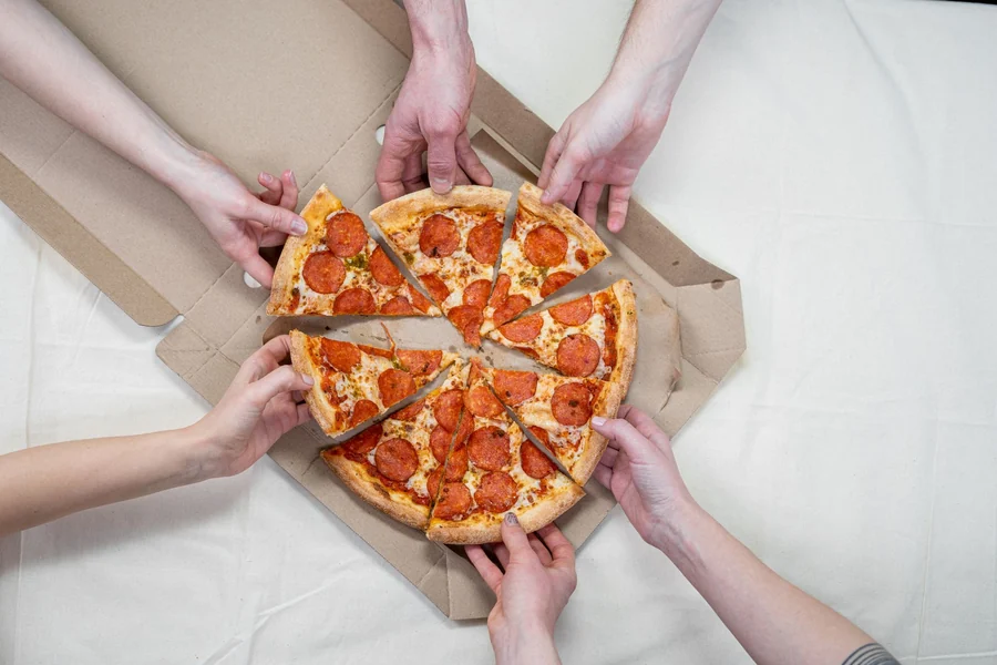 Double cut pizza - several hands reaching for slices of pizza on a table