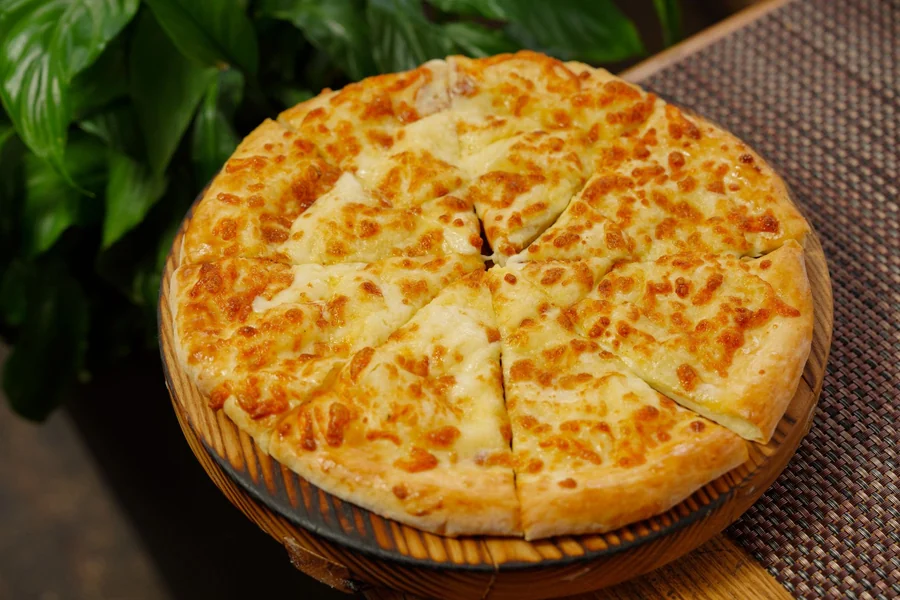 Double cut pizza - whole cheese pizza on a wooden board ready to slice