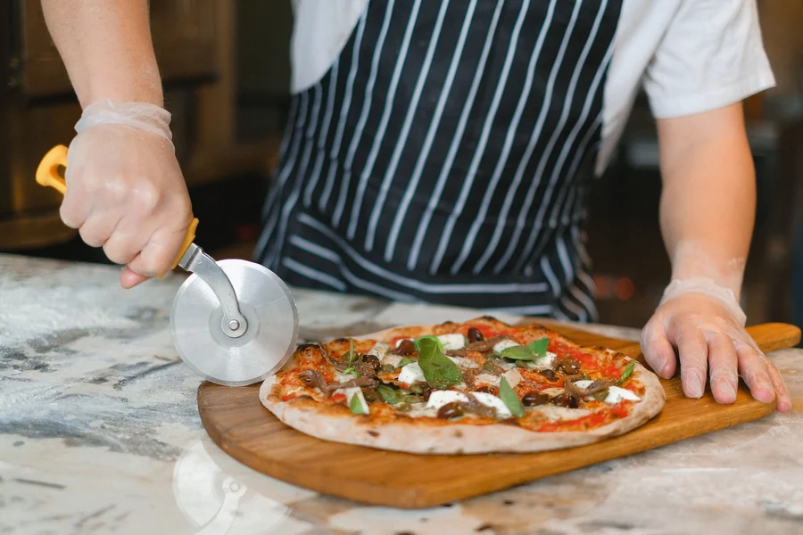 Double cut pizza - chef using a pizza cutter wheel to slice a pizza