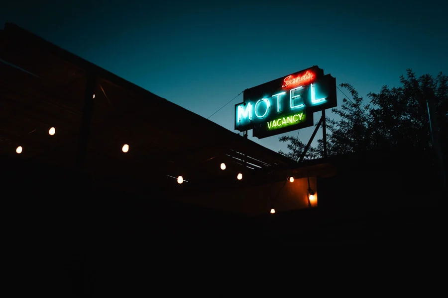John Candy net worth - classic neon motel sign glowing at dusk