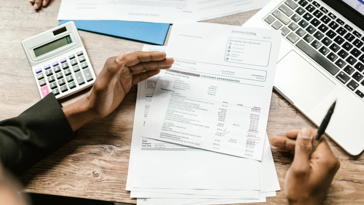 Hands holding financial documents beside a calculator and laptop at a desk