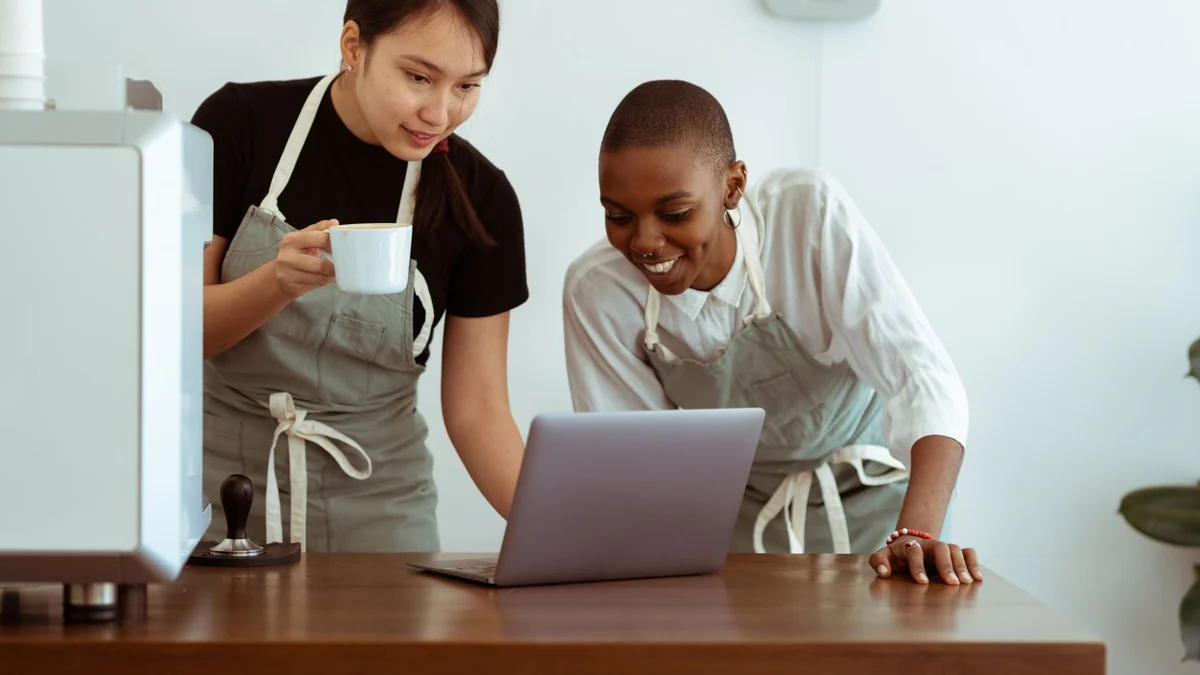 Two cafe staff reviewing figures together on a laptop behind the counter
