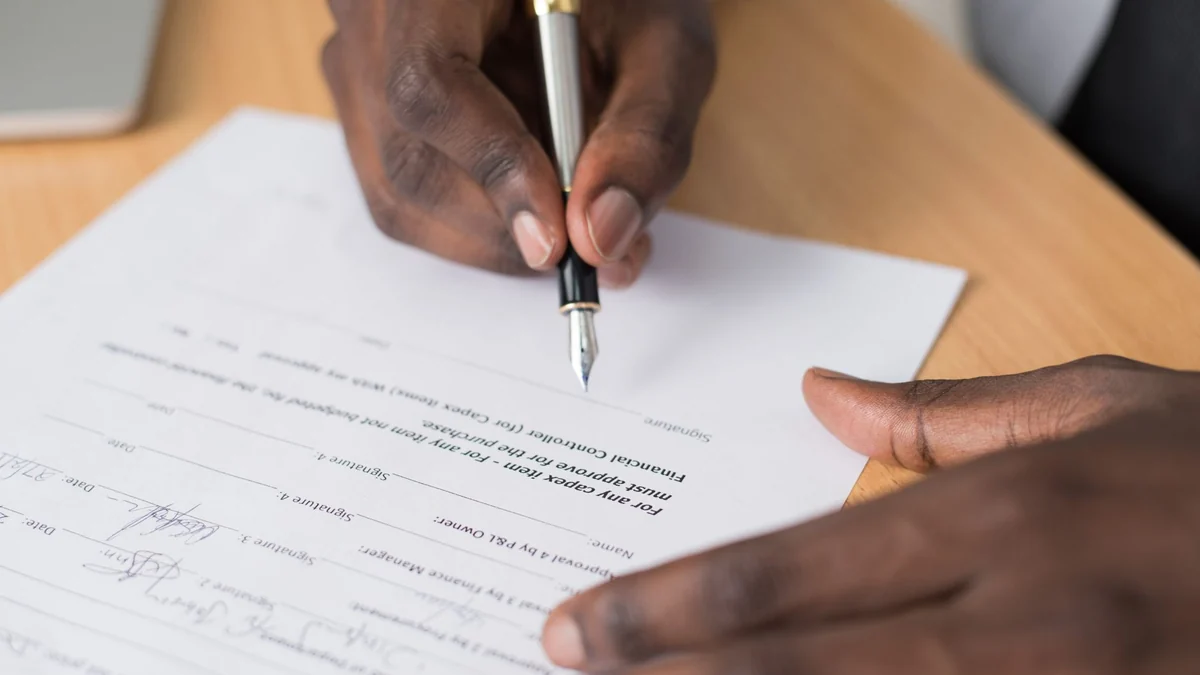A person signing a contract with a pen at a wooden desk
