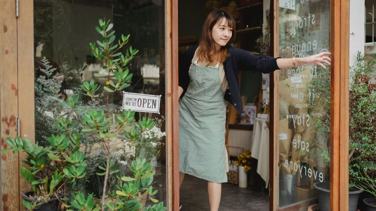 A shop owner in an apron opening the door of a small independent shop