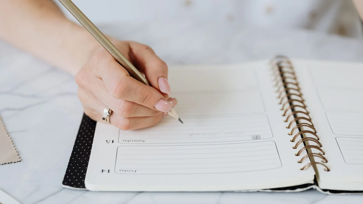 Close-up of a hand writing notes in a planner to track skin flare-ups and treatments
