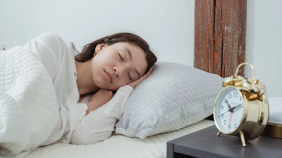 A woman sleeping peacefully on her side in a white bed with a bedside alarm clock