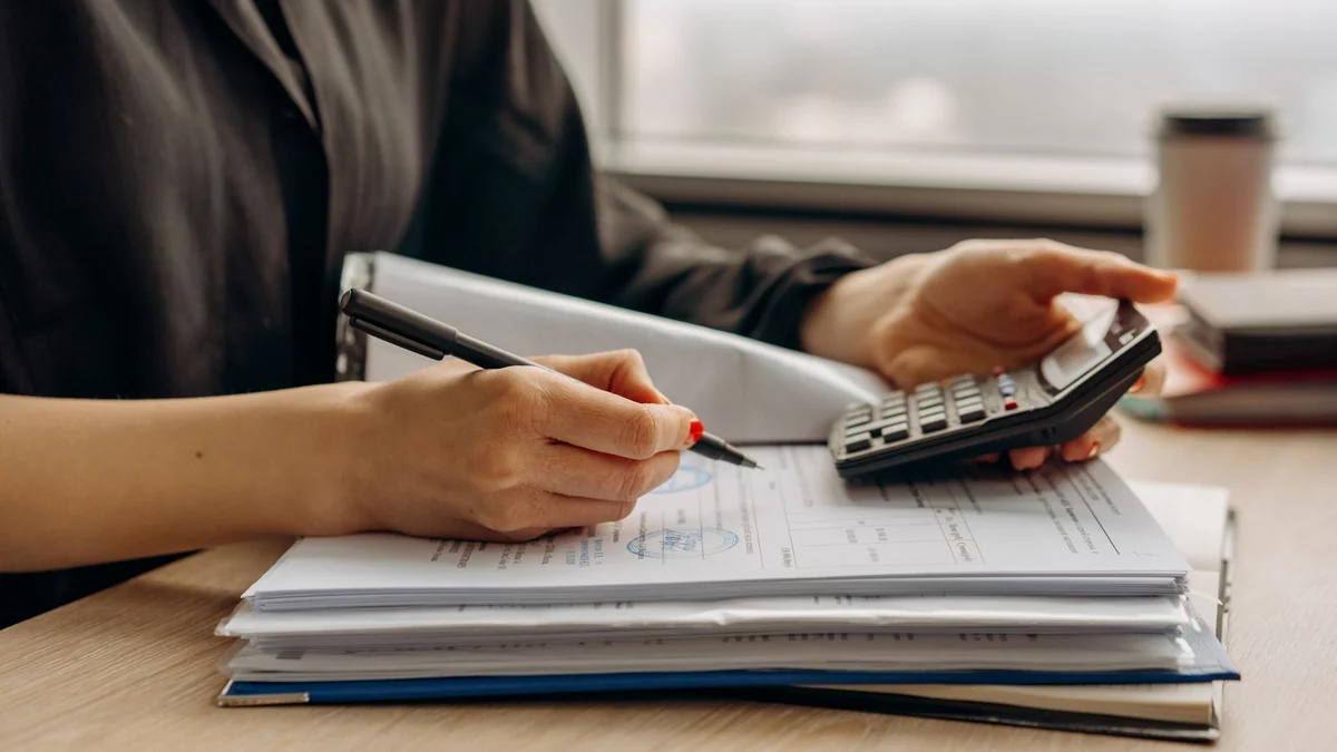 A person using a calculator beside financial documents at a desk