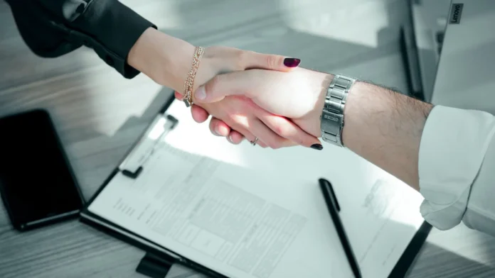 London Business for Sale: How to Finance the Purchase (UK Guide) Two people shaking hands over a signed contract and clipboard to close a business purchase