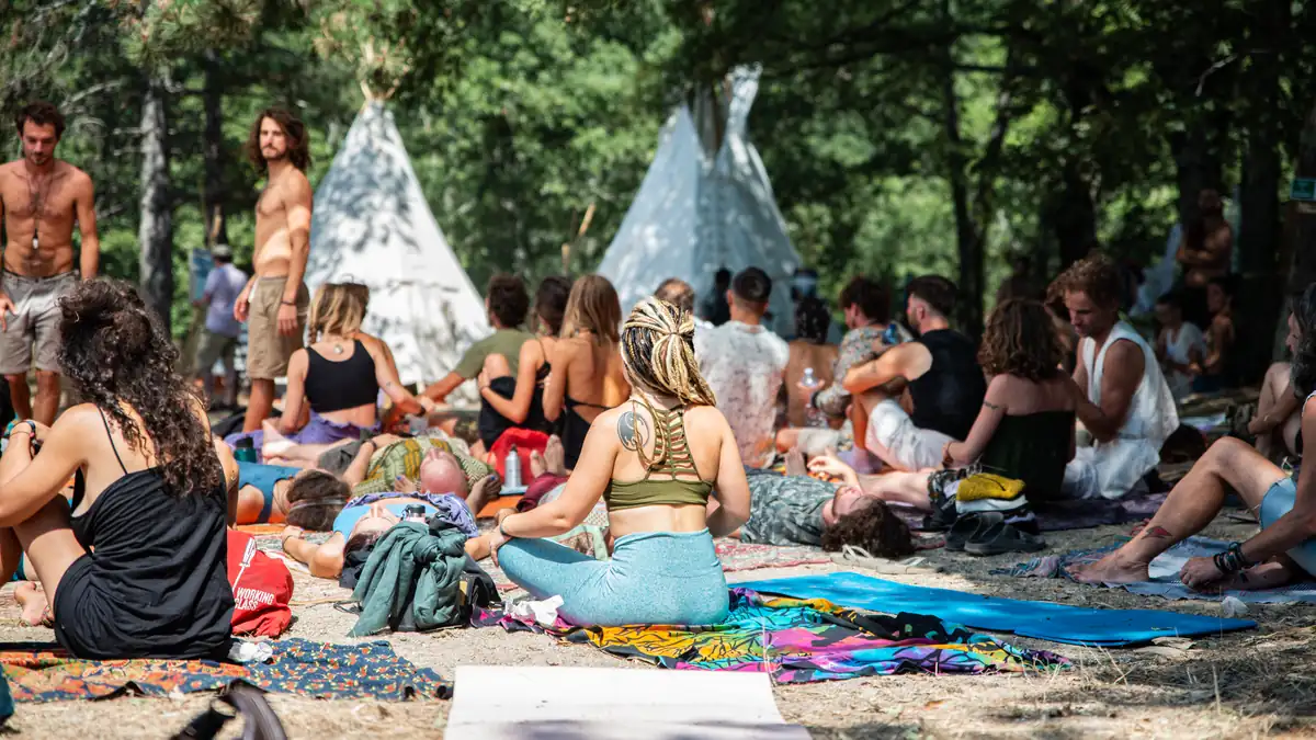 A group of people relaxing and exercising on mats under trees at an outdoor wellness festival